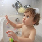A child palying with soap foam in a bathtub.